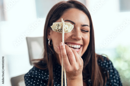 Shot of funny business woman holding gyoza with chopsticks while having lunch in the office photo