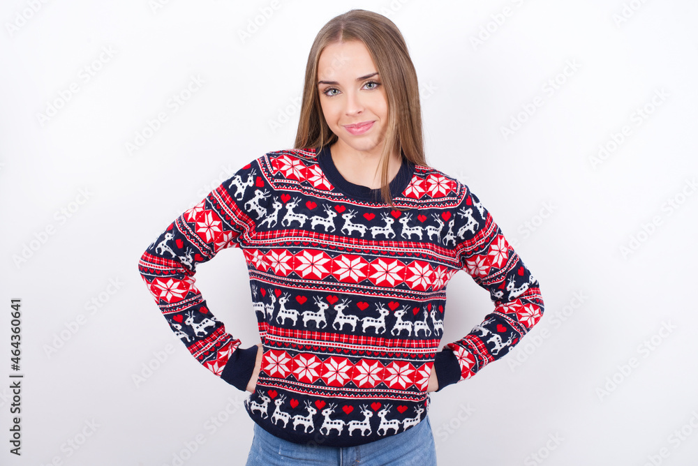 Funny frustrated Young beautiful caucasian girl wearing christmas sweaters on white background holding hands on waist and silly looking at awkward situation. Funny frustrated Young beautiful caucasian girl wearing christmas sweaters on white background holding hands on waist and silly looking at awkward situation.