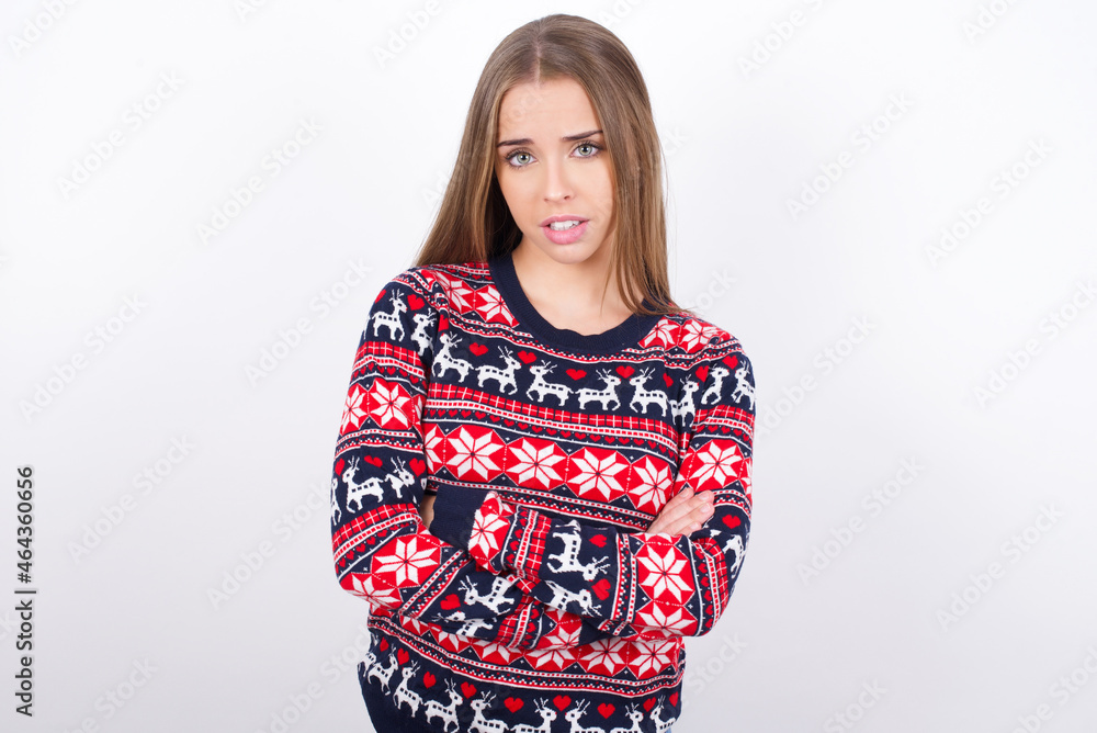 Young beautiful caucasian girl wearing christmas sweaters on white background frowning his face in displeasure, keeping arms folded, waiting for an explanation. Young beautiful caucasian girl wearing christmas sweaters on white background frowning his face in displeasure, keeping arms folded, waiting for an explanation.