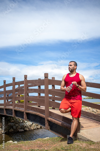 Fototapeta Naklejka Na Ścianę i Meble -  Athletic young man refreshing himself with water after running in blue sky natural landscape background. Healthy lifestyle