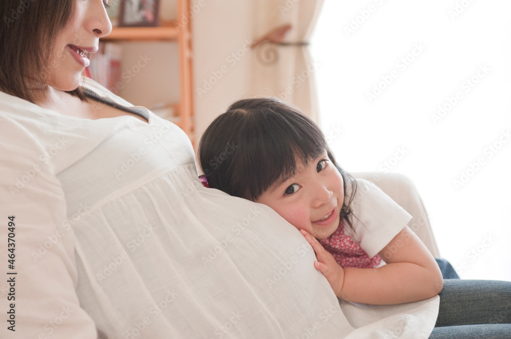 リビングで妊婦のお母さんのお腹を触る女の子 リビングで妊婦のお母さんのお腹を触る女の子