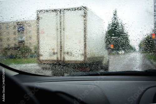 Road and rain on the glass of a car, overtaking a truck, a traffic light is visible.