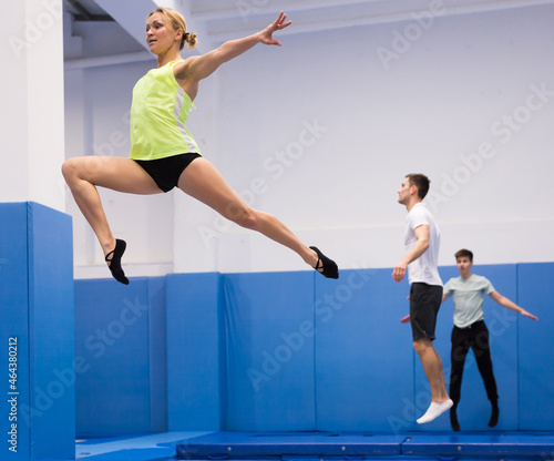 Young athletic woman exercising acrobatic elements in jump on trampoline in sports center..