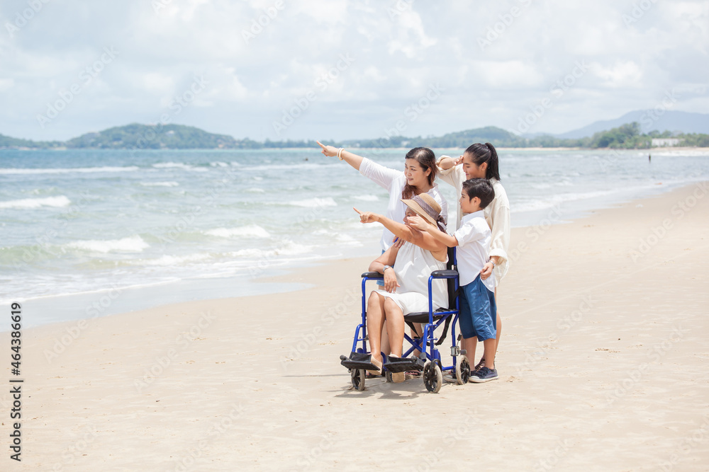 Disabled woman asia in a wheelchair with his family on the beach. Wheelchair woman sitting relax on the beach. family relax concept Disabled woman asia in a wheelchair with his family on the beach. Wheelchair woman sitting relax on the beach. family relax concept