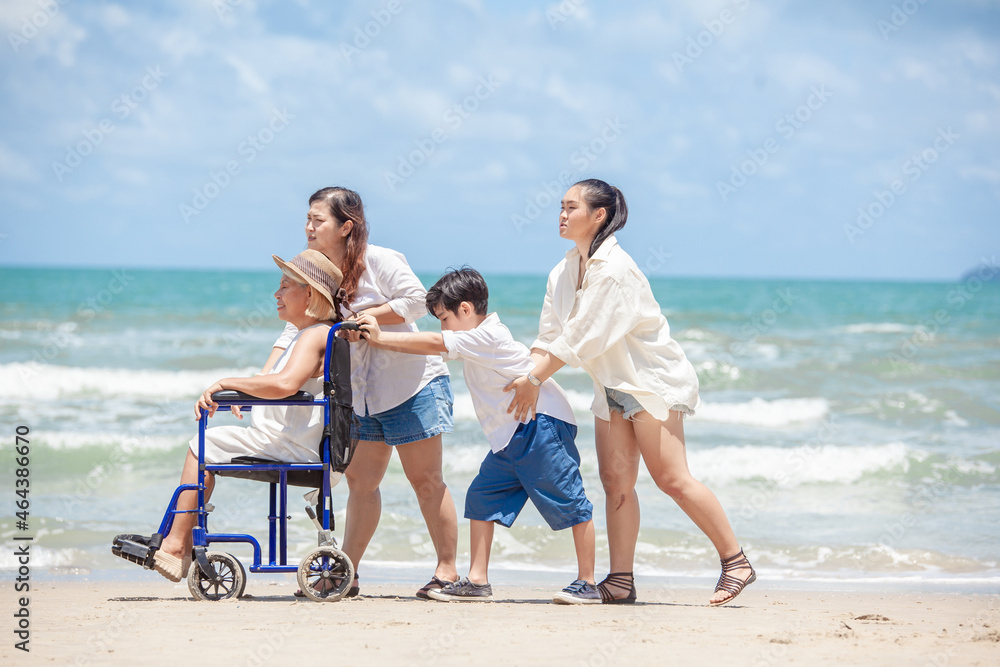 Disabled woman asia in a wheelchair with his family on the beach. Wheelchair woman sitting relax on the beach. family relax concept Disabled woman asia in a wheelchair with his family on the beach. Wheelchair woman sitting relax on the beach. family relax concept