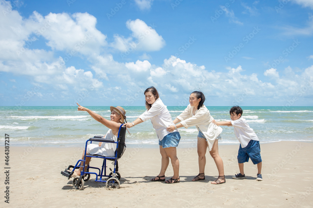 Disabled woman asia in a wheelchair with his family on the beach. Wheelchair woman sitting relax on the beach. family relax concept Disabled woman asia in a wheelchair with his family on the beach. Wheelchair woman sitting relax on the beach. family relax concept