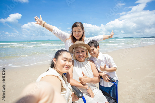 Disabled woman asia in a wheelchair with his family on the beach. Wheelchair woman sitting relax on the beach. Happy family taking selfie on sea beach