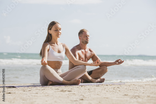 Young couple practicing yoga on the sea beach at sunset. Doing yoga - meditating and relaxing in beach