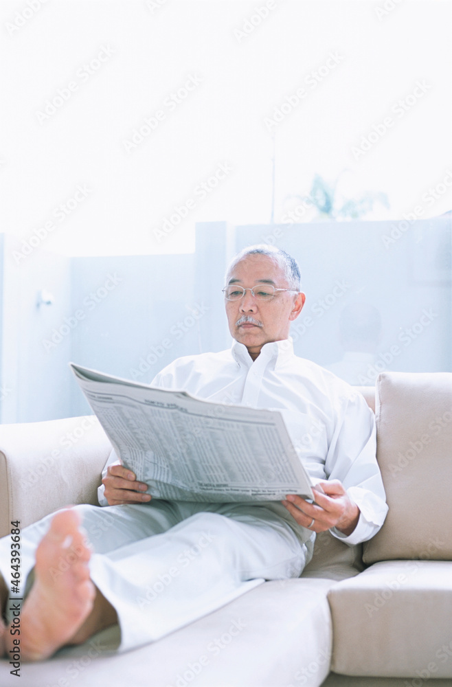 ソファーで新聞を読む中高年男性 ソファーで新聞を読む中高年男性