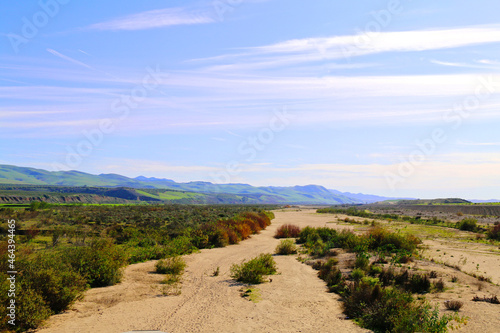 dry riverbed sandy deserted desert land with mountains and hills under a blue cloudy sky