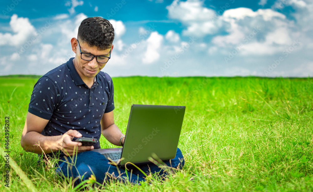 Young man in glasses working on his laptop, man in the field with his computer Young man in glasses working on his laptop, man in the field with his computer