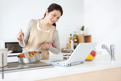ノートパソコンを見ながら料理する女性