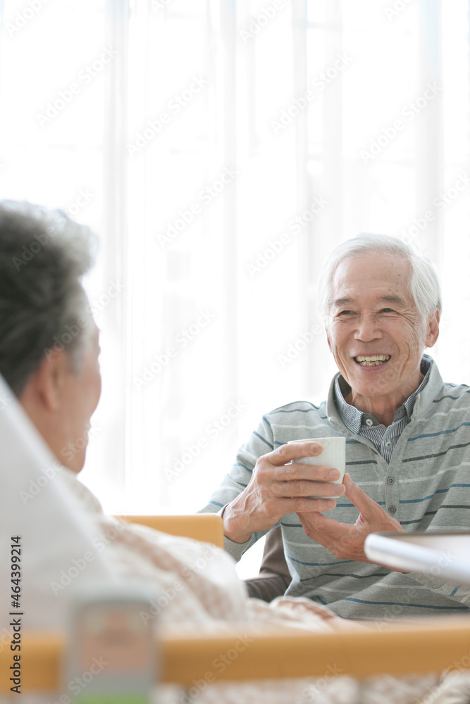 介護ベッドに横になる妻とお茶を飲む夫 介護ベッドに横になる妻とお茶を飲む夫