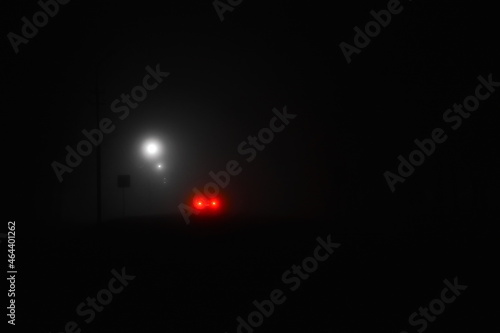 mystical dense fog on night street lit by lanterns, the red light of the car's brake light is burning, dark night cityscape with black copy space