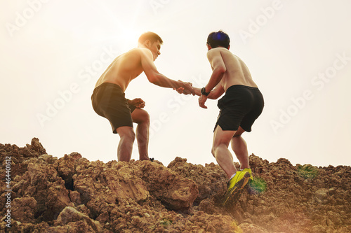 Silhouette of trail runner with hand helping each other hike up a mountain top together with sunset background. Help and support concept.