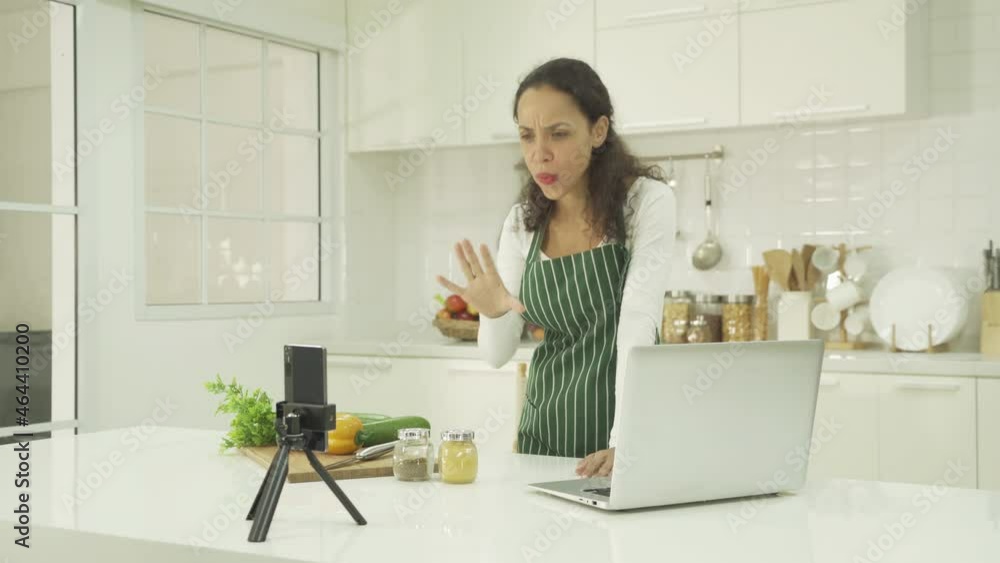 Portrait of happy smiling, latin woman talking, cooking food at home, video live on webcam video meeting with computer laptop, call conference, working online in kitchen. People lifestyle. Webinar Portrait of happy smiling, latin woman talking, cooking food at home, video live on webcam video meeting with computer laptop, call conference, working online in kitchen. People lifestyle. Webinar