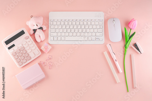 Top view of cute feminine soft pastel pink theme desktop workspace which consists of calculator, notebook, pens, mouse, keyboard, stapler, small teddy bear and a pink tulip. With copyspace.