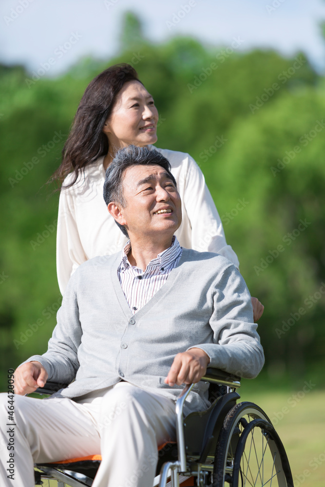 車椅子に乗る中高年男性と押して歩く中高年女性 車椅子に乗る中高年男性と押して歩く中高年女性