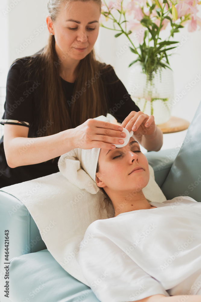 beautician makes facial and massage to a young woman with a towel on her head beautician makes facial and massage to a young woman with a towel on her head