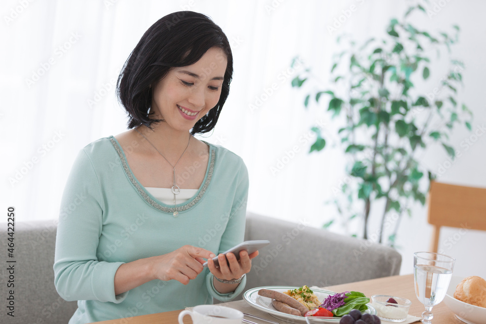 朝食中にスマートフォンを操作する女性 朝食中にスマートフォンを操作する女性