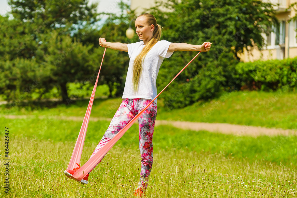 Girl doing exercises outdoor, using resistance fit band.