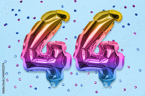 Rainbow foil balloon number, digit forty four on a blue background with sequins. Birthday greeting card with inscription 44. Top view. Numerical digit. Celebration event, template. photo