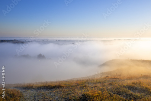 Autumn landscape in the early morning. Fog-covered expanses through which the first rays of the rising sun pass. Trees and hills in the fog. Dawn on a cold autumn morning.