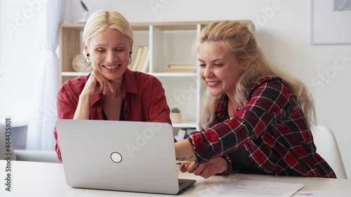 Online learning. Family study. Individual training. Language course. Amused mature mother daughter watching fun video lesson together using laptop in light home interior. photo