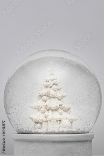 Close up of a white Christmas snow globe with white Christmas tree decorated with presents and gifts. White background with copy space available.