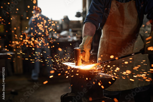 Billede på lærred Close-up of blacksmith in apron working with hammer and iron in the workshop
