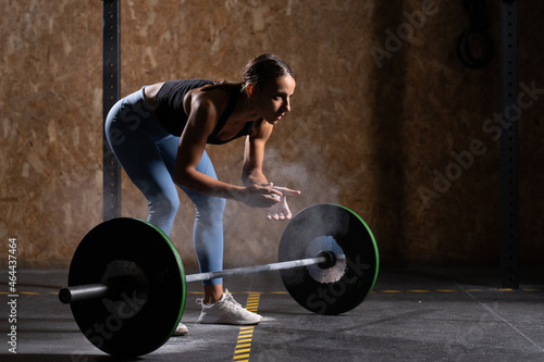 Concentrated fit woman clapping hands with chalk before lifting a heavy barbell.