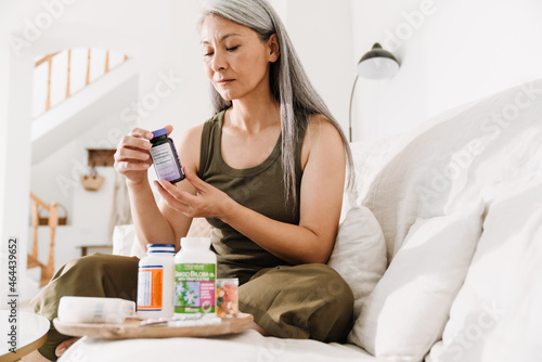 Mature asian woman taking her medication while sitting on couch photo