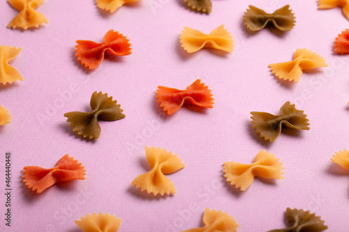 Pattern made of uncooked farfalle tricolore pasta on pastel pink background. Macaroni background. Top view, flat lay. © alexburakov12