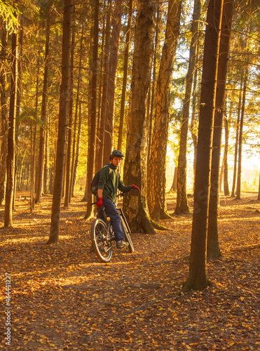  A young man in a helmet on a sports bike in the forest, illuminated by sunlight.
