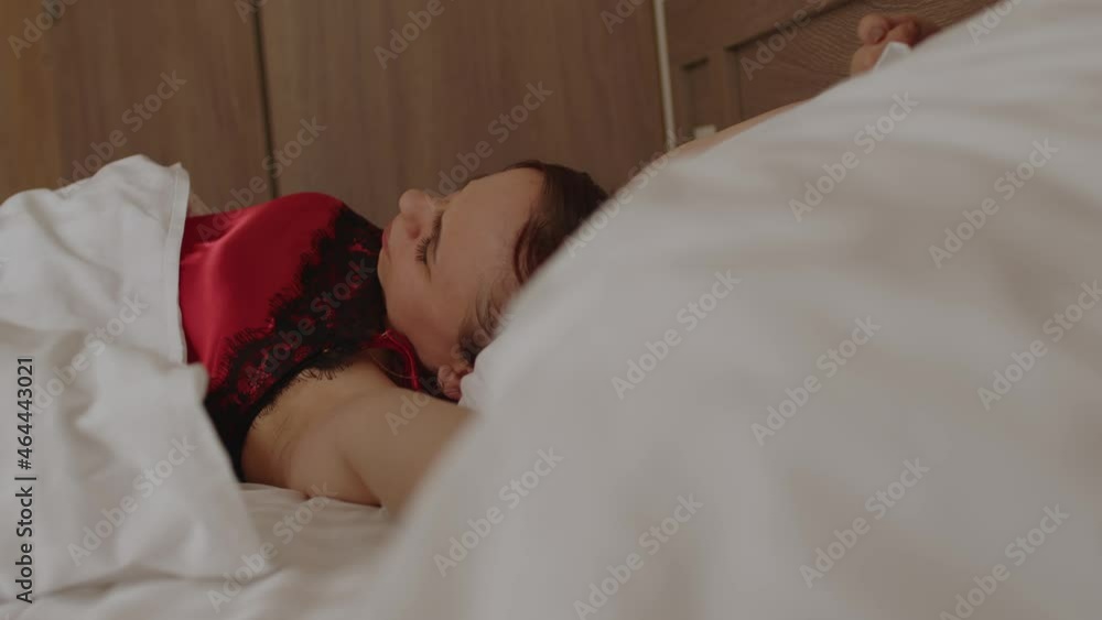 Young woman under blanket sleeping on bed in morning. Sleepy female wakes up and yawns, lying on pillow. Young woman under blanket sleeping on bed in morning. Sleepy female wakes up and yawns, lying on pillow.