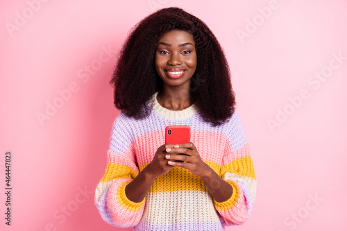 Photo of charming dark skin girl beaming smile hold phone look camera isolated on pink color background