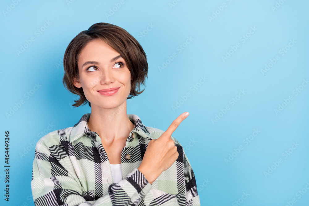 Photo of funny dreamy young woman dressed checkered shirt pointing finger empty space smiling isolated blue color background Photo of funny dreamy young woman dressed checkered shirt pointing finger empty space smiling isolated blue color background