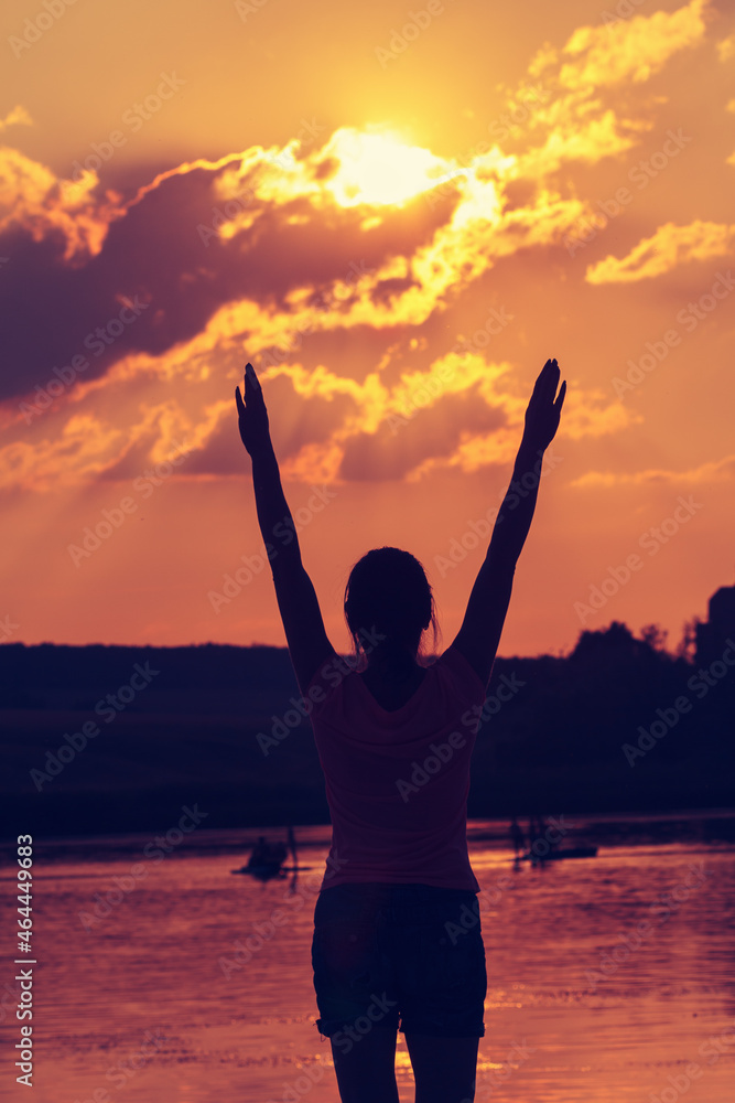 Silhouette of a young woman with arms raised in the backdrop of the setting sun