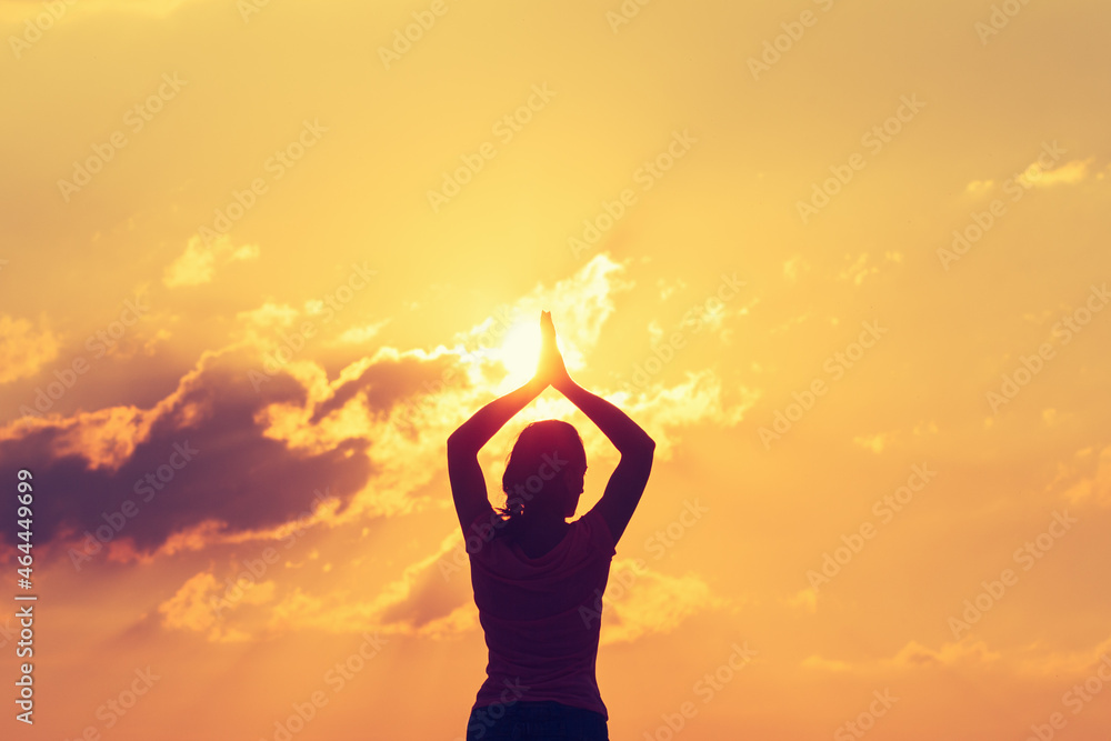Young woman does yoga or fitness at sunset. Silhouette on the background sun.