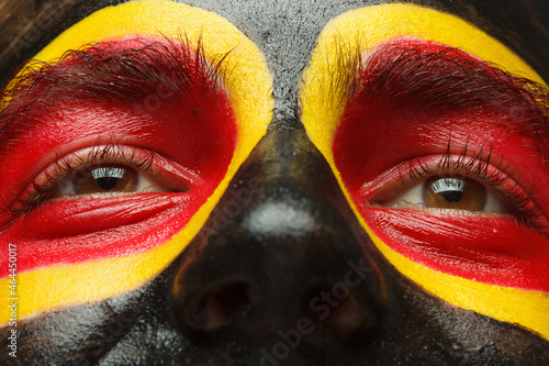 Eyes of German or Belgian sports fan patriot. Painted country flag on man face.
