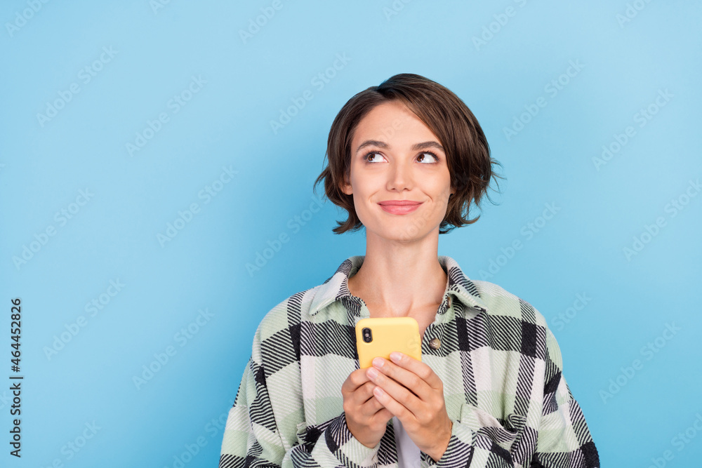 Photo of interested millennial brunette lady look empty space hold telephone wear plaid shirt isolated on blue color background