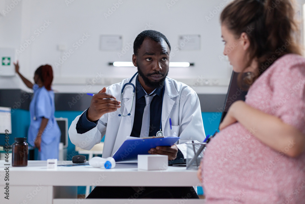 Obraz premium Medical physician consulting woman expecting child at desk in cabinet. General practitioner talking to pregnant patient about pregnancy and healthcare, specialist giving advice.