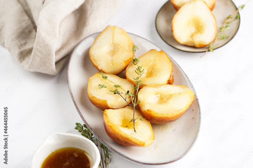 Caramelized pear halves on an oval grey plate with thyme branches and caramel on a white table surface