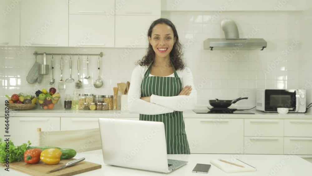 Portrait of happy smiling latin woman using a computer laptop notebook technology device, cooking food, working online at home in kitchen. People lifestyle. Household Portrait of happy smiling latin woman using a computer laptop notebook technology device, cooking food, working online at home in kitchen. People lifestyle. Household