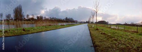 panorama of a bicycle path in autumnal light with a river along it at dusk with a cloudy sky photo