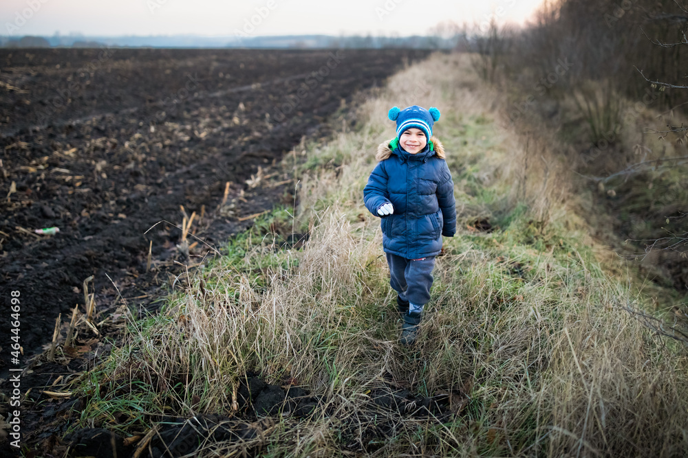 Little preschool boy running in winter clothes along the field in village Little preschool boy running in winter clothes along the field in village