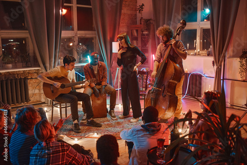 Group of young people playing musical instruments and singing during performance for people in the studio