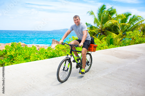 Happy young guy riding a bike on the road by the sea in the Seychelles. Concept of vacation and active lifestyle. Cycling. The man on the bike.