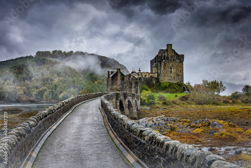 Moody autumn view of the Eilean Donan Castle in the Highlands of Scotland with misty mountains and rain clouds