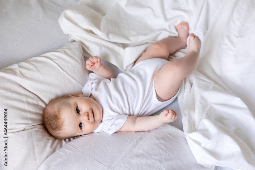 baby in a white bodysuit is lying on his back in a bed made with white bed linen. children's sleep and rest. concept of a happy childhood and motherhood. lifestyle, space for text. High quality photo baby in a white bodysuit is lying on his back in a bed made with white bed linen. children's sleep and rest. concept of a happy childhood and motherhood. lifestyle, space for text. High quality photo